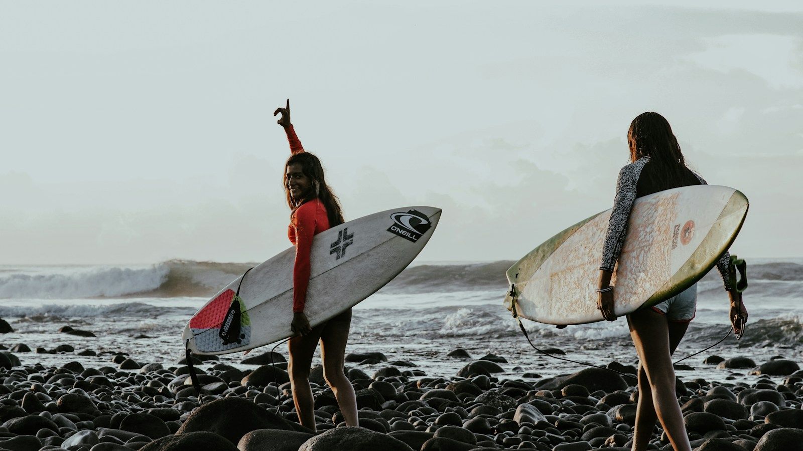 Two surfers carrying boards on the rocky shore at Playa El Tunco